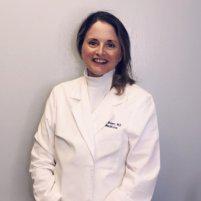 A woman in white coat standing next to wall.