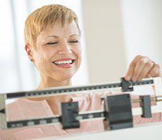 A woman smiles while standing on a scale.