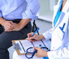 A doctor is writing on paper while another person sits next to him.